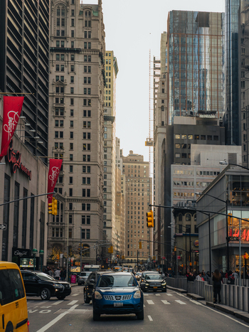 View of traffic moving through a busy street in Manhattan surrounded by tall skyscrapers and historic architecture in New York New York United States.