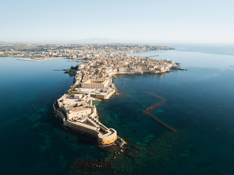 Aerial view of the Island of Ortigia featuring Maniace Castle and historic rooftops surrounded by the turquoise Mediterranean sea in Syracuse Sicily Italy. Aerial view of the Island of Ortigia featuring Maniace Castle and historic rooftops surrounded by the turquoise Mediterranean sea in Syracuse Sicily Italy.