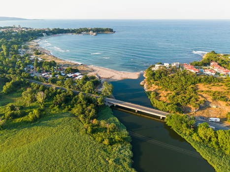 Aerial view of Kiten South Beach where the river meets the Black Sea featuring a bridge crossing the river lush green vegetation and coastal buildings in Kiten Burgas Bulgaria. Aerial view of Kiten South Beach where the river meets the Black Sea featuring a bridge crossing the river lush green vegetation and coastal buildings in Kiten Burgas Bulgaria.