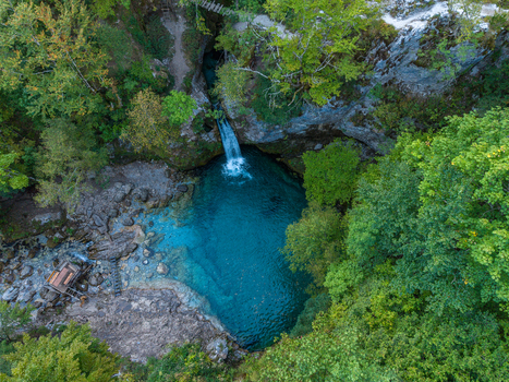Aerial view of Blue Eye Theth featuring a vibrant turquoise natural pool fed by a waterfall surrounded by lush green forest and rocky terrain in Theth Shkoder County Albania. Aerial view of Blue Eye Theth featuring a vibrant turquoise natural pool fed by a waterfall surrounded by lush green forest and rocky terrain in Theth Shkoder County Albania.