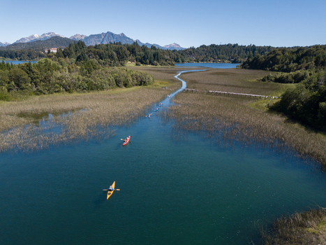 Aerial view of people kayaking on the blue waters of Nahuel Huapi Lake surrounded by green reeds and lush forests with mountains in San Carlos de Bariloche Rio Negro Argentina. Aerial view of people kayaking on the blue waters of Nahuel Huapi Lake surrounded by green reeds and lush forests with mountains in San Carlos de Bariloche Rio Negro Argentina.