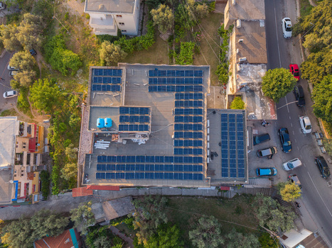 Aerial view of solar panels on a building rooftop surrounded by lush trees and a street with parked cars in Kruje Durres County Albania.