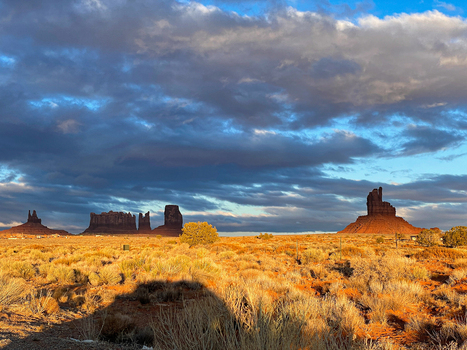 View of Monument Valley Tribal Park with iconic red sandstone buttes desert scrub and dramatic clouds at sunset in Oljato Monument Valley Utah United States.