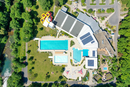 Aerial view of Konigsbad Forchheim with outdoor swimming pools water slides and solar panels on roofs surrounded by lush green trees in Forchheim Bayern Germany. Aerial view of Konigsbad Forchheim with outdoor swimming pools water slides and solar panels on roofs surrounded by lush green trees in Forchheim Bayern Germany.
