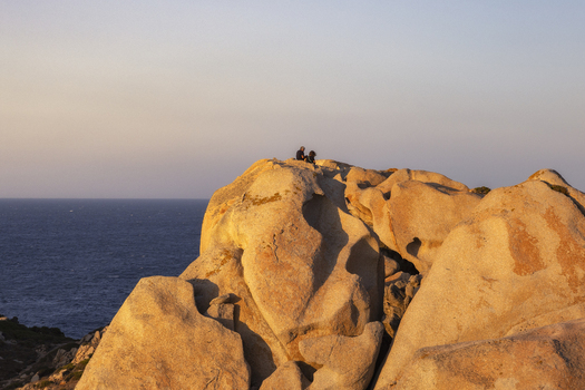 View of Capo Testa granite rock formations with two people sitting on the summit overlooking the Mediterranean Sea during golden hour Capo Testa Sardegna Italy. View of Capo Testa granite rock formations with two people sitting on the summit overlooking the Mediterranean Sea during golden hour Capo Testa Sardegna Italy.