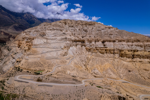 Aerial view of a winding mountain road carved into the arid layered slopes of the Himalayas under a clear blue sky in Nepal.