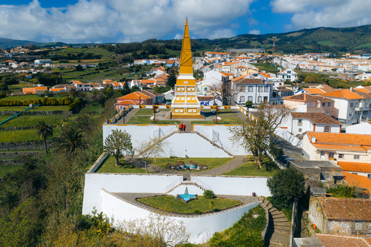 Aerial view of the Alto da Memoria monument with its yellow obelisk and tiered gardens overlooking the historic city and green hills Angra do Heroismo Azores Portugal.