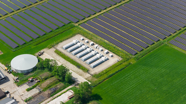 Aerial view of a large solar panel farm with a battery energy storage system and a circular tank surrounded by green fields in Wanneperveen Overijssel Netherlands. Aerial view of a large solar panel farm with a battery energy storage system and a circular tank surrounded by green fields in Wanneperveen Overijssel Netherlands.