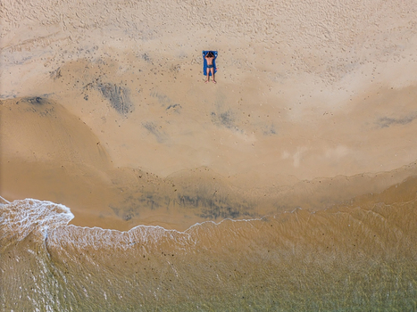 Aerial view of a person sunbathing on a blue towel on a sandy beach with gentle waves washing ashore in Cascais Lisbon Portugal. Aerial view of a person sunbathing on a blue towel on a sandy beach with gentle waves washing ashore in Cascais Lisbon Portugal.