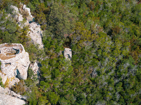 Aerial view of the historic stone structure at Passo del Monumento surrounded by dense Mediterranean forest and rocky terrain in Campo nell Elba Toscana Italy.