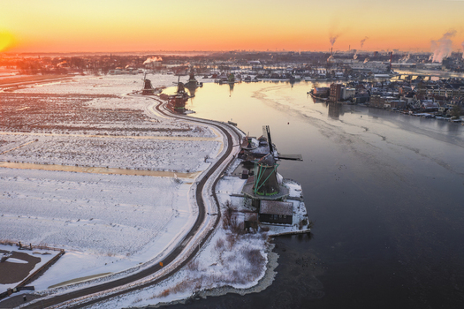 Aerial view of the historic Zaanse Schans windmills along a snow covered riverbank during a golden sunset in Zaandam Noord Holland Netherlands. Aerial view of the historic Zaanse Schans windmills along a snow covered riverbank during a golden sunset in Zaandam Noord Holland Netherlands.