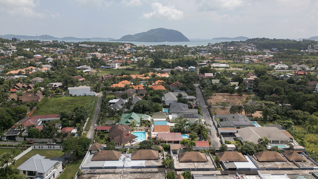 Aerial view of a residential neighborhood in Thailand featuring houses with tiled roofs private swimming pools lush tropical vegetation and a distant coastline with islands. Aerial view of a residential neighborhood in Thailand featuring houses with tiled roofs private swimming pools lush tropical vegetation and a distant coastline with islands.
