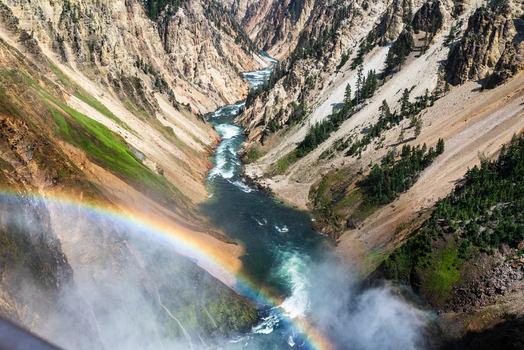 Aerial view of the Grand Canyon of the Yellowstone with the Yellowstone River flowing through steep canyon walls pine trees and a rainbow in the mist in Cody Wyoming United States. Aerial view of the Grand Canyon of the Yellowstone with the Yellowstone River flowing through steep canyon walls pine trees and a rainbow in the mist in Cody Wyoming United States.