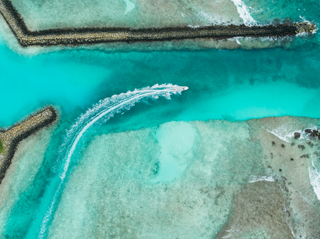 Aerial view of a boat sailing through turquoise waters between stone breakwaters leaving a white wake trail Vashafaru Island Thiladhummathi Atoll Maldives. Aerial view of a boat sailing through turquoise waters between stone breakwaters leaving a white wake trail Vashafaru Island Thiladhummathi Atoll Maldives.
