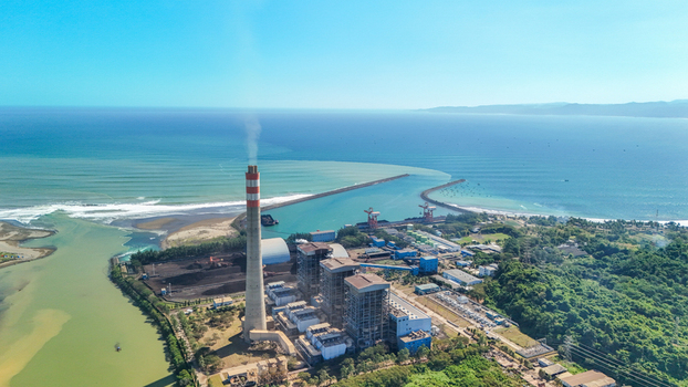 Aerial view of a power plant with a tall chimney and industrial facilities situated on the coast near the sea in Indonesia.
