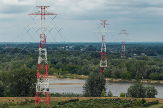 Aerial view of red and white electricity pylons crossing a river and lush green landscape in Poland. Aerial view of red and white electricity pylons crossing a river and lush green landscape in Poland.