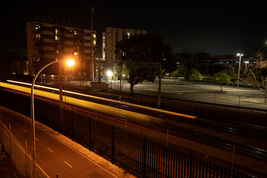 View of a train moving along the tracks at night with light trails illuminated buildings and street lighting in the background in Perth Western Australia Australia.