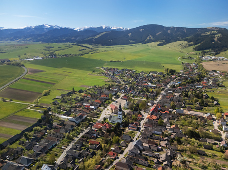 Aerial view of the historic village of Partizanska Lupca with its church tower green fields and the snow capped Low Tatra mountains Partizanska Lupca Zilina Region Slovakia.