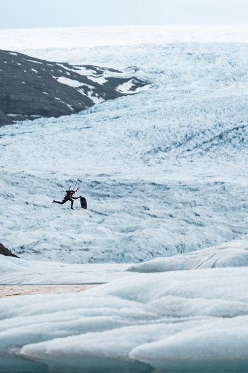 View of a kiteboarder performing a jump over the icy terrain of the Vatnajokull glacier in Iceland.