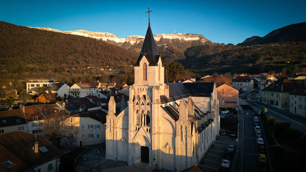 Aerial view of Eglise Saint Pierre with its tall steeple and the surrounding town houses against the snow capped Jura mountains in Gex Auvergne Rhone Alpes France. Aerial view of Eglise Saint Pierre with its tall steeple and the surrounding town houses against the snow capped Jura mountains in Gex Auvergne Rhone Alpes France.