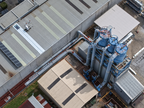 Aerial view of industrial factory complex featuring large blue storage silos extensive piping systems and corrugated metal rooftops in Melbourne VIC Australia.