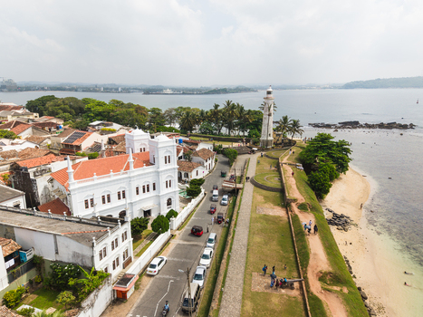 Aerial view of the historic Galle Lighthouse and Meeran Mosque along the coastal ramparts with people walking near the beach in Galle Southern Province Sri Lanka. Aerial view of the historic Galle Lighthouse and Meeran Mosque along the coastal ramparts with people walking near the beach in Galle Southern Province Sri Lanka.