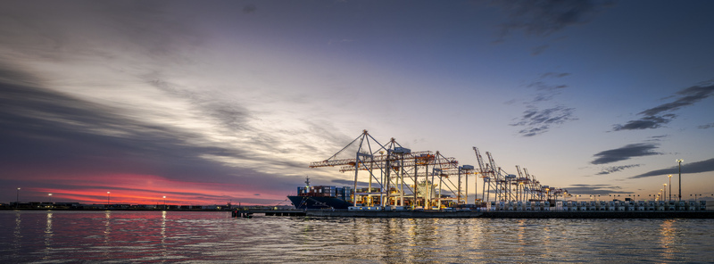 View of Port of Tauranga Ltd at Sulphur Point with a large container ship docked under giant cranes during a vibrant sunset over the water in Tauranga Bay of Plenty Region New Zealand.