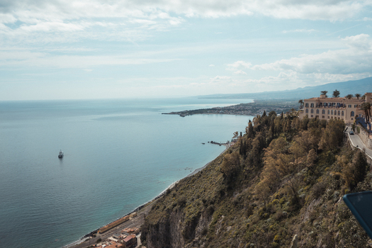 View of the azure sea meets the rugged coastline where historic buildings cling to the cliffs under a serene sky Taormina Sicily Italy.