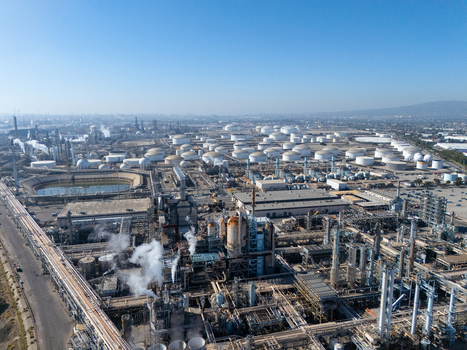 Aerial view of an industrial oil refinery featuring numerous storage tanks complex piping systems and processing units under a clear blue sky in Carson California United States.