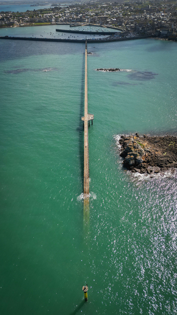 Aerial view of the long pier stretching into the turquoise sea connecting to the rocky outcrop of Île de Batz Roscoff Brittany France. Aerial view of the long pier stretching into the turquoise sea connecting to the rocky outcrop of Île de Batz Roscoff Brittany France.