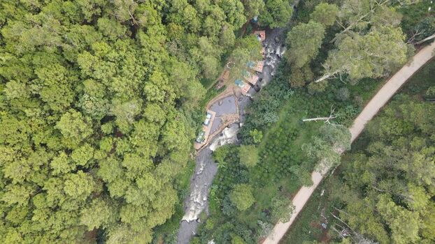 Aerial view of Hutan Pinus Rahong featuring a winding river flowing through dense pine forest with a dirt path running alongside in Pangalengan West Java Indonesia. Aerial view of Hutan Pinus Rahong featuring a winding river flowing through dense pine forest with a dirt path running alongside in Pangalengan West Java Indonesia.
