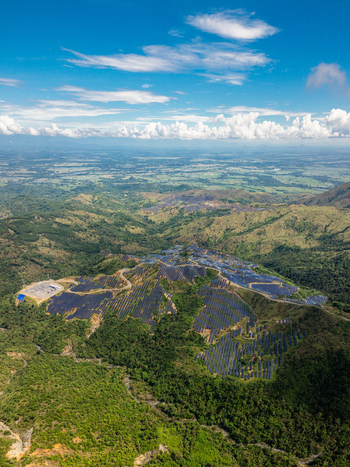 Aerial view of a large solar farm installed on a lush green mountain slope under a blue sky with white clouds in Aguilar Ilocos Region Philippines.