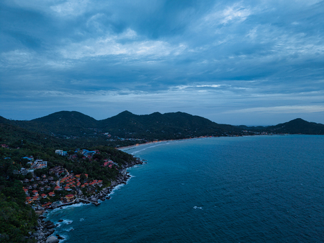 Aerial view of Ko Tao coastline at twilight with illuminated resorts nestled among lush green hills along the dark blue sea in Ko Tao Surat Thani Thailand.