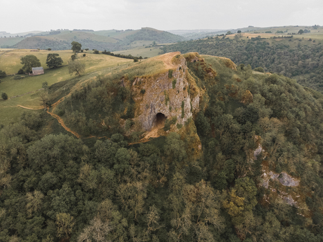 Aerial view of Thor s Cave set within the rolling green hills and limestone cliffs of the Peak District in Ashbourne England United Kingdom.