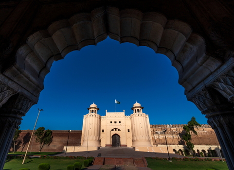 View of the historic Lahore Fort with its iconic gate stone walls and the flag of Pakistan against a clear blue sky framed by an arch in Lahore Punjab Pakistan.