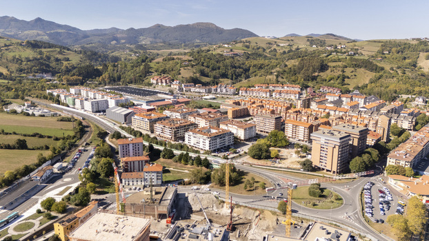 Aerial view of the town of Zumaia featuring residential apartment buildings a construction site with cranes a roundabout and surrounding green hills in Zumaia Basque Country Spain.