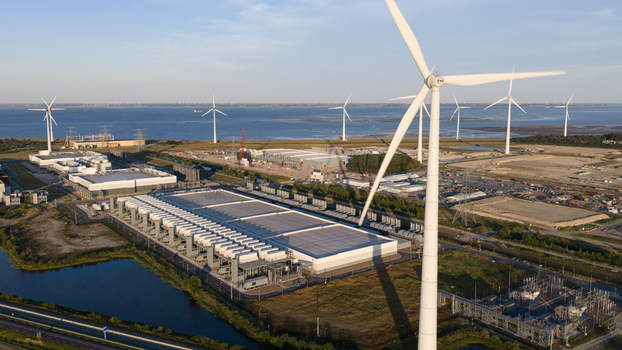 Aerial view of a large industrial data center complex with expansive rooftops and cooling infrastructure surrounded by wind turbines and coastal landscape in Eemshaven Groningen Netherlands.