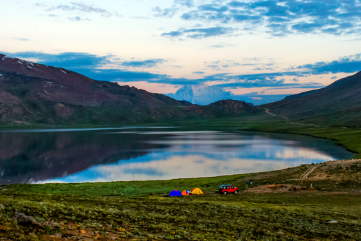 View of Sheosar Lake at twilight with colorful tents and a vehicle parked on the grassy shore surrounded by majestic mountains in Skardu Pakistan. View of Sheosar Lake at twilight with colorful tents and a vehicle parked on the grassy shore surrounded by majestic mountains in Skardu Pakistan.