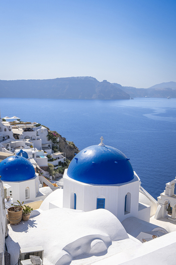 View of iconic blue domed churches with white washed architecture overlooking the Aegean Sea in Fira Greece.