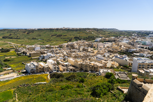 View of the town of Zebbug with light colored stone houses and green agricultural fields under a clear blue sky in Zebbug Gozo Region Malta. View of the town of Zebbug with light colored stone houses and green agricultural fields under a clear blue sky in Zebbug Gozo Region Malta.