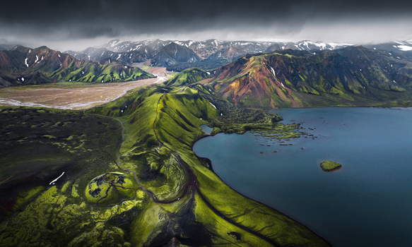 Aerial view of the vibrant green mossy mountains and deep blue lake of Landmannalaugar under a dramatic stormy sky Iceland.