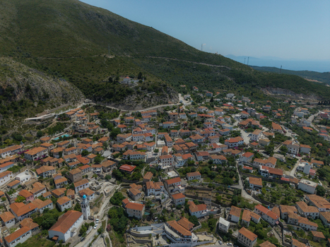 Aerial view of the coastal village of Dhermi featuring traditional red tiled rooftops white houses and a church with a blue dome nestled against green hills in Dhermi Vlore County Albania. Aerial view of the coastal village of Dhermi featuring traditional red tiled rooftops white houses and a church with a blue dome nestled against green hills in Dhermi Vlore County Albania.