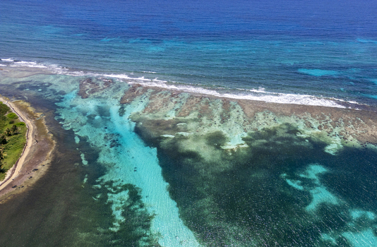 Aerial view of the vibrant coral reefs and turquoise waters along the lush tropical coastline Guanaja Bay Islands Department Honduras. Aerial view of the vibrant coral reefs and turquoise waters along the lush tropical coastline Guanaja Bay Islands Department Honduras.