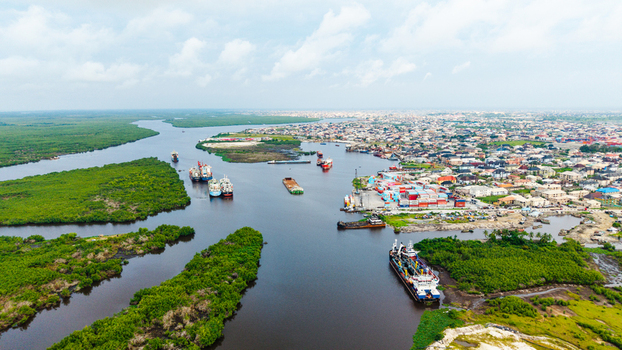 Aerial view of Satellite Town featuring industrial port facilities cargo ships navigating the waterway and surrounding mangrove forests in Lagos Lagos Nigeria.