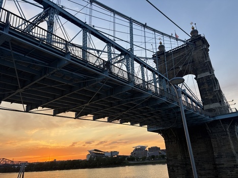 View of the John A. Roebling Suspension Bridge with its blue steel cables and stone towers against a vibrant sunset sky Covington Kentucky United States.