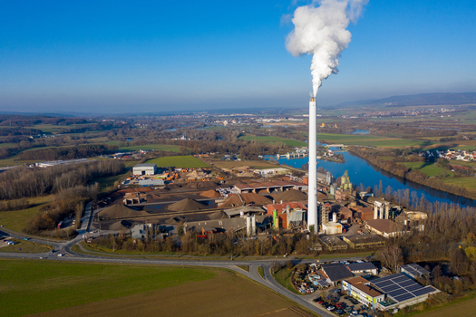 Aerial view of the Liapor GmbH Co. KG industrial plant with a tall chimney emitting smoke near the Regnitz river and autumn fields in Hallerndorf Bayern Germany. Aerial view of the Liapor GmbH Co. KG industrial plant with a tall chimney emitting smoke near the Regnitz river and autumn fields in Hallerndorf Bayern Germany.