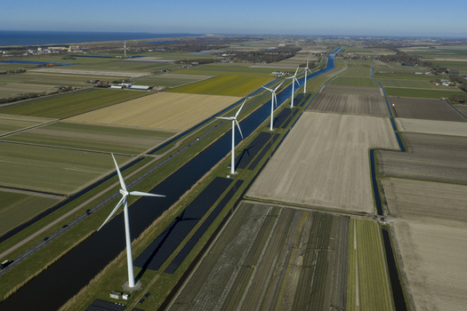 Aerial view of a row of modern wind turbines and solar panels along a straight canal through flat agricultural fields under a clear blue sky Netherlands. Aerial view of a row of modern wind turbines and solar panels along a straight canal through flat agricultural fields under a clear blue sky Netherlands.