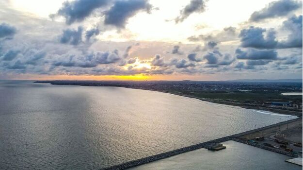 Aerial view of the coastline at sunset with calm waters a long breakwater and dramatic clouds over the horizon in Ghana. Aerial view of the coastline at sunset with calm waters a long breakwater and dramatic clouds over the horizon in Ghana.