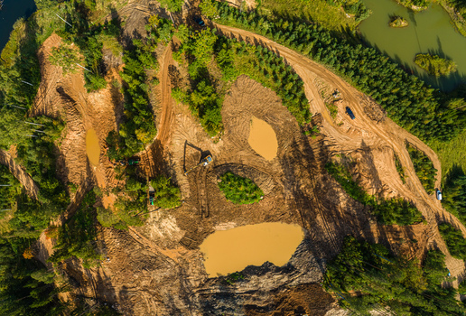 Aerial view of an excavation site with muddy ground pools of water and an excavator surrounded by forest in Latvia. Aerial view of an excavation site with muddy ground pools of water and an excavator surrounded by forest in Latvia.