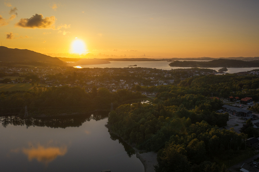 Aerial view of Hommersak at sunset featuring the golden sun reflecting over the calm waters of the bay surrounded by lush green forests and coastal residential areas in Hommersak Rogaland Norway. Aerial view of Hommersak at sunset featuring the golden sun reflecting over the calm waters of the bay surrounded by lush green forests and coastal residential areas in Hommersak Rogaland Norway.